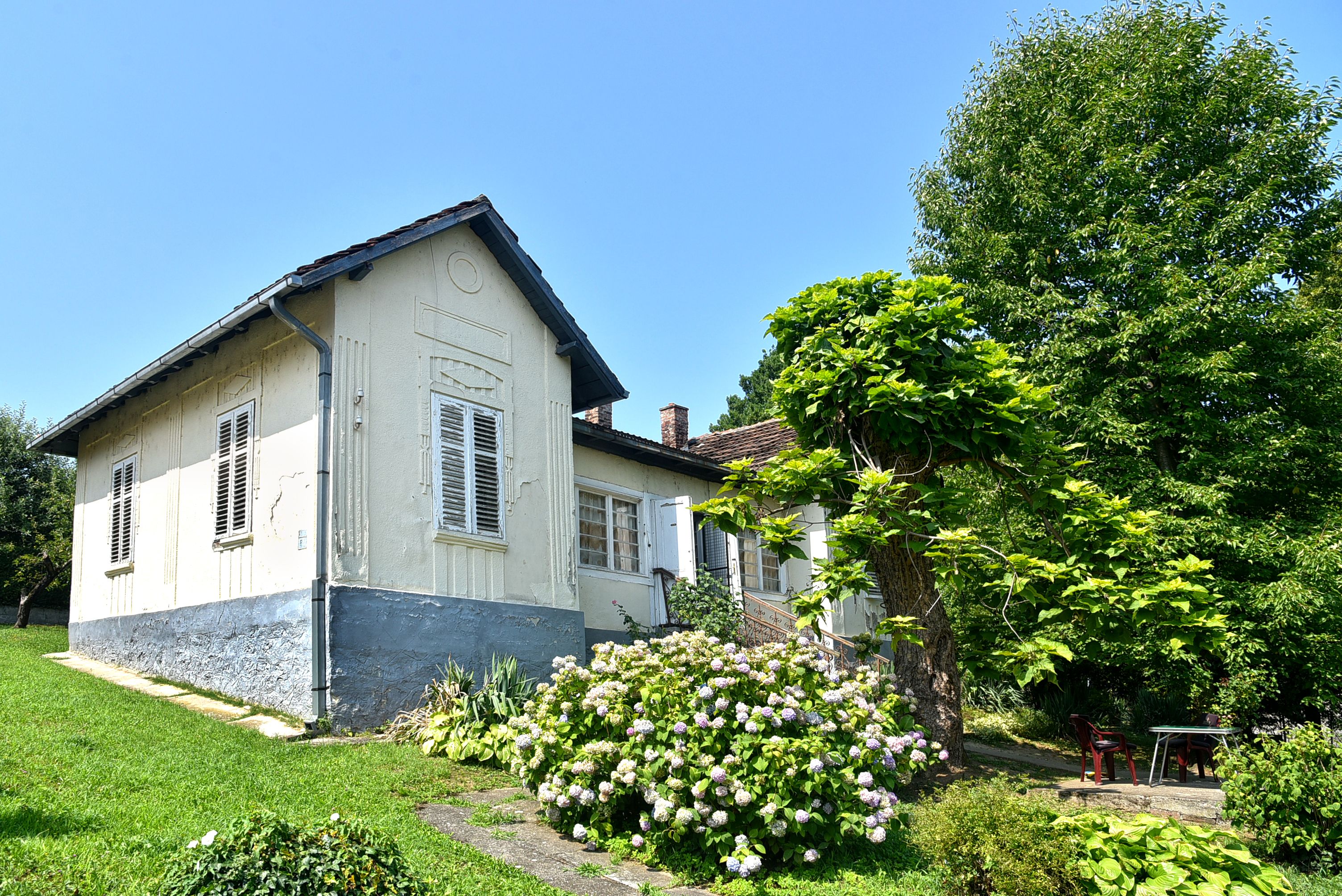 Vila Danica, mala prizemna kuća sa svetlom fasadom, zelenim travnjakom i cvetnim žbunjem