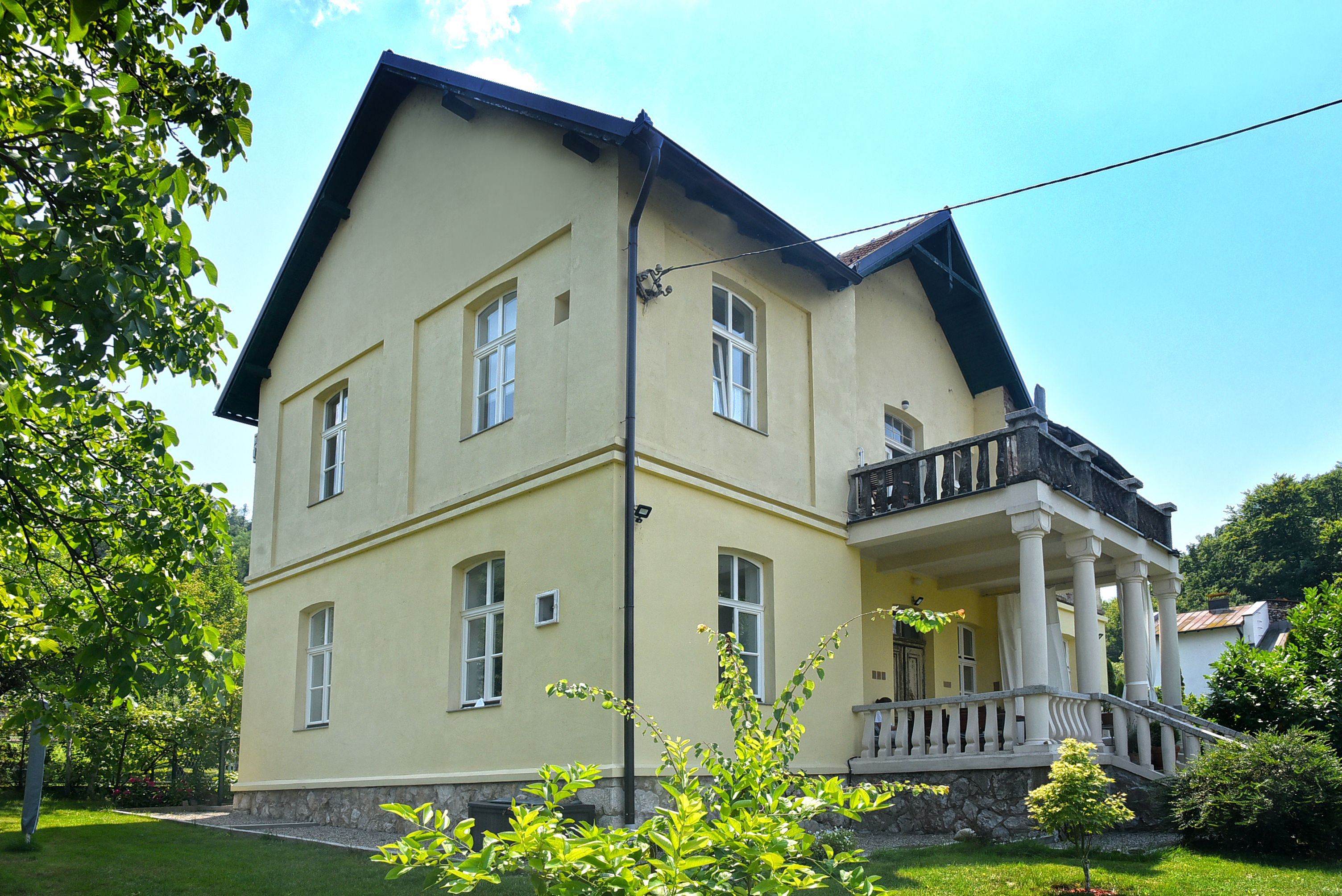 Vila Gučevo sa žutom fasadom, tremom na stubovima i terasom iznad ulaza, u zelenom dvorištu